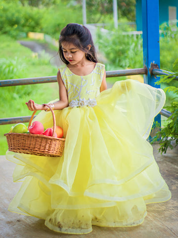 Young girl in a yellow dress holding a basket of apples outdoors. by fashion designers in pune