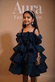 Young girl wearing a navy blue ruffled dress with 'Aura Fashion' branding in the background by fashion designers in pune