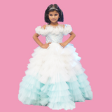 Young girl in a white and light blue dress with ruffled layers on a pink background by kids fashion designers in pune