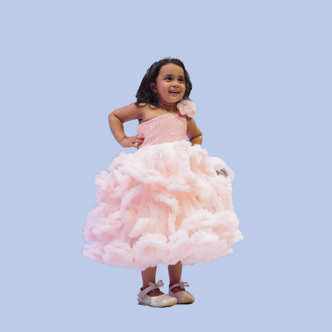 Child wearing a pink dress with a fluffy skirt against a light blue background by best fashion designer in pune