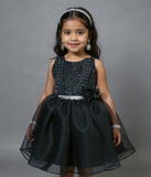 Young girl wearing a black dress with silver accents against a gray background by fashion designers in pune