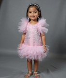 Young girl in a pink dress with ruffled sleeves and skirt on a gray background by kids dress designers in pune