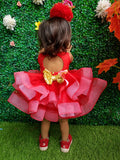 Child wearing a red dress with a gold bow in front of a green wall with flowers.
