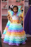 Child wearing a colorful dress with a rainbow skirt in front of a mirror by fashion designers in pune